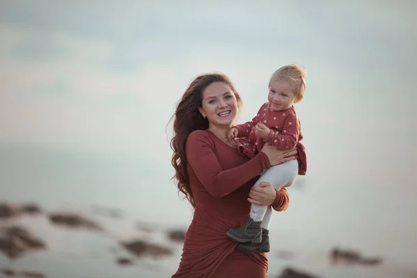Ein kleines Mädchen und eine Mutter gehen am Meer spazieren, sie spielen und umarmen sich — Stockfoto