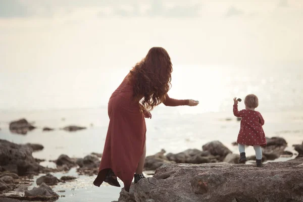Ein kleines Mädchen und eine Mutter gehen am Meer spazieren, sie spielen und werfen Steine ins Wasser — Stockfoto