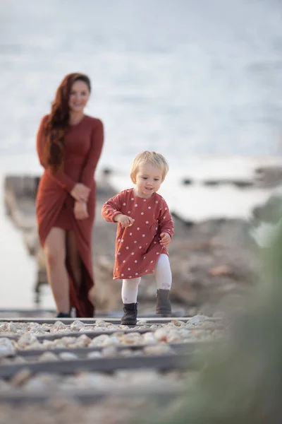Een klein meisje en mama lopen vlak bij de zee, ze spelen en knuffelen — Stockfoto