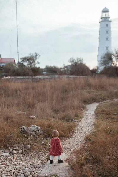 一个小女孩沿着小路走到灯塔边，在秋海边散步 — 图库照片