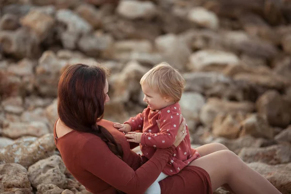 Porträt einer glücklichen Mutter und Tochter, Mutter umarmt ein kleines Mädchen auf dem Hintergrund der Steine — Stockfoto