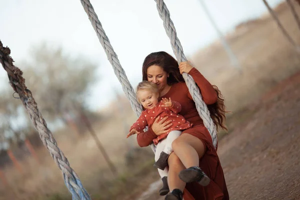 幸せなお母さんと娘は夏の自然を背景に車輪でスイング. — ストック写真