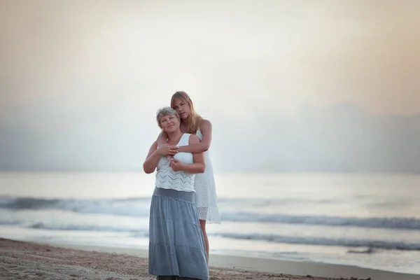Portrait of a happy mother and adult daughter. They hug on the background of the sea. — Stok fotoğraf
