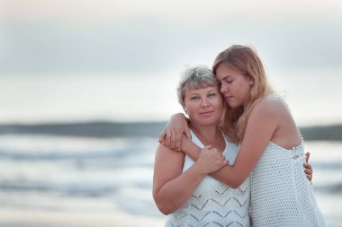 Portrait of a happy mother and adult daughter. They hug on the background of the sea.