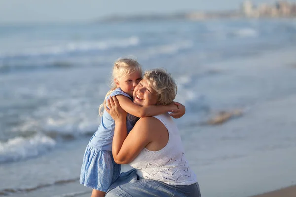 Porträt einer glücklichen Mutter und einer kleinen Tochter. sie umarmen sich auf dem Hintergrund des Meeres. — Stockfoto
