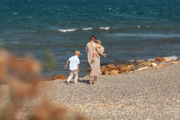 Pretty happy mom and little children on a walk near the sea — 图库照片
