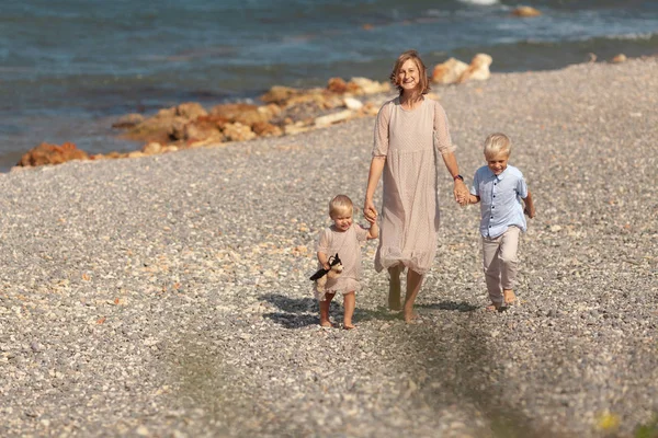 Pretty happy mom and little children on a walk near the sea — Stok fotoğraf