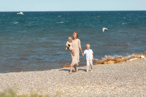 Pretty happy mom and little children on a walk near the sea — Stok fotoğraf