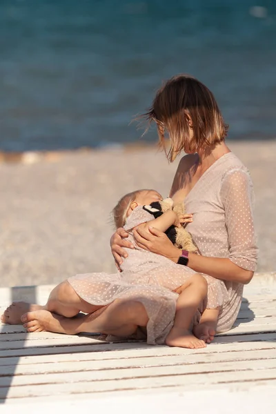 Bela mãe feliz amamentando criança pequena na costa do mar , — Fotografia de Stock