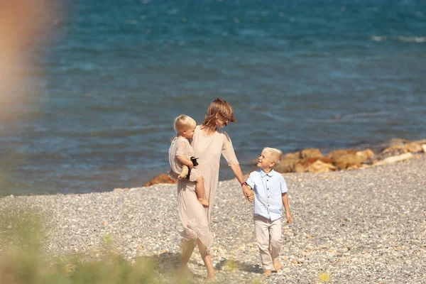 Pretty happy mom and little children on a walk near the sea — Stok fotoğraf