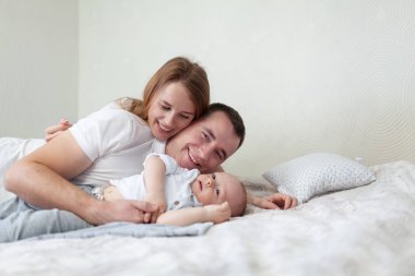 Mutlu genç bir ailenin portresi. Aileler ve bebekler odada kanepede sarılıp oynuyorlar.