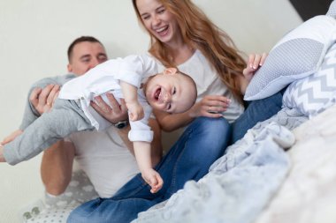 Mutlu genç bir ailenin portresi. Aileler ve bebekler odada kanepede sarılıp oynuyorlar.