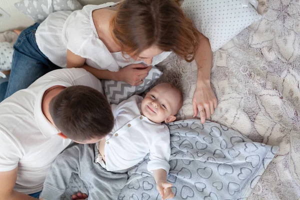 幸せな若い家族の肖像画。両親と赤ちゃんは抱き合って部屋のソファで遊んでいます — ストック写真