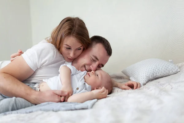 幸せな若い家族の肖像画。両親と赤ちゃんは抱き合って部屋のソファで遊んでいます — ストック写真