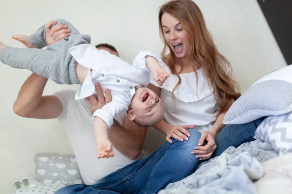 Portret młodej, szczęśliwej rodziny. Rodzice i dziecko przytulają się i bawią na kanapie w pokoju — Zdjęcie stockowe