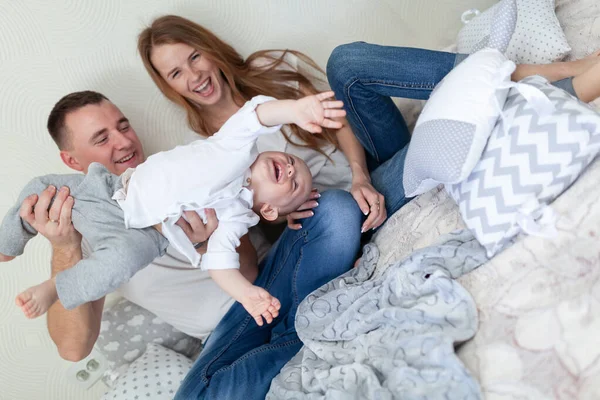 Retrato de uma jovem família feliz. Pais e bebê abraçando e brincando no sofá da sala — Fotografia de Stock