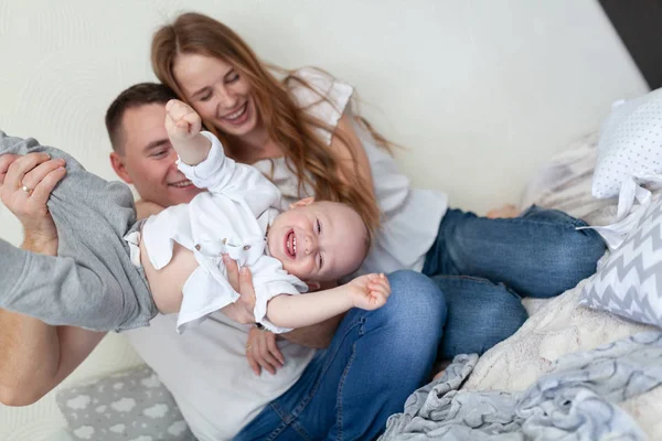 Retrato de uma jovem família feliz. Pais e bebê abraçando e brincando no sofá da sala — Fotografia de Stock