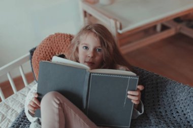 Kapalı bir odada, kanepede kitap okuyan bir kız.