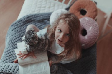 Kapalı bir odada, kanepede kitap okuyan bir kız.