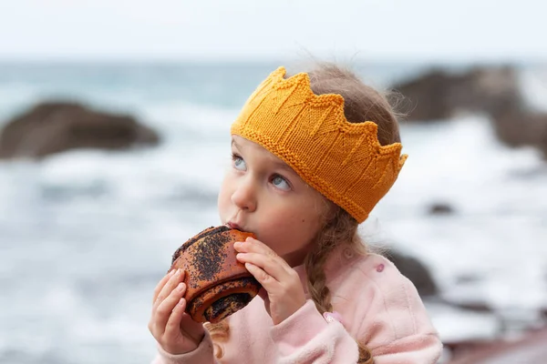 Ein Mädchen Isst Vor Dem Hintergrund Des Meeres Ein Brötchen — Stockfoto