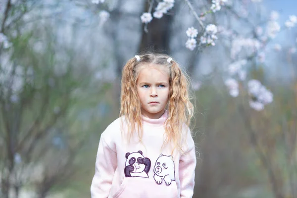一个美丽而严肃的小女孩的画像 背景是盛开的粉色杏仁 — 图库照片
