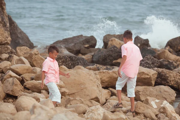 两个兄弟在海滨玩耍 他们穿着珊瑚衬衫 在水里扔石头 — 图库照片