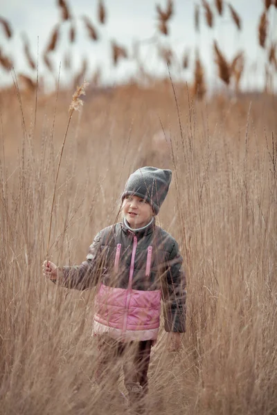 Cute little girl staying among reed at first sunny spring day and looking cheerfully, happy family weekend, outdoor closeup portrait, child plays fun in the reeds