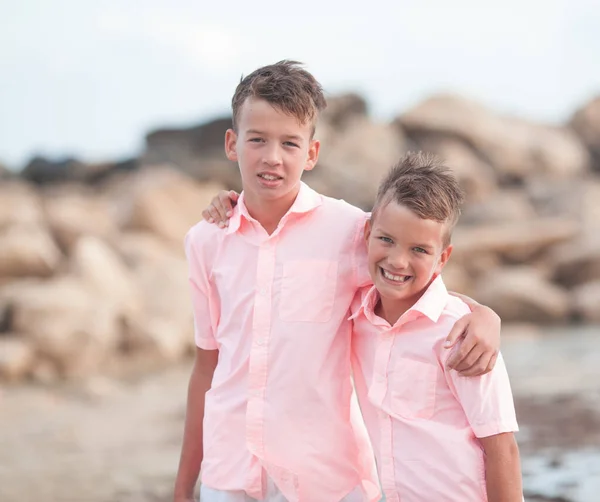 Portrait of two happy brothers brothers in coral shirts on a background of stones and the sea, outdoor