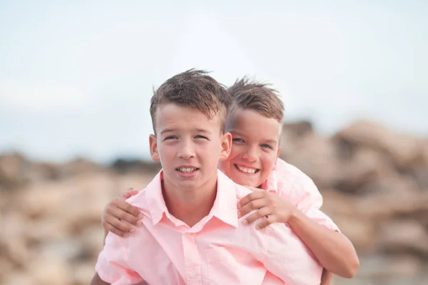 石や海を背景にサンゴのシャツを着た2人の幸せな兄弟の肖像 — ストック写真