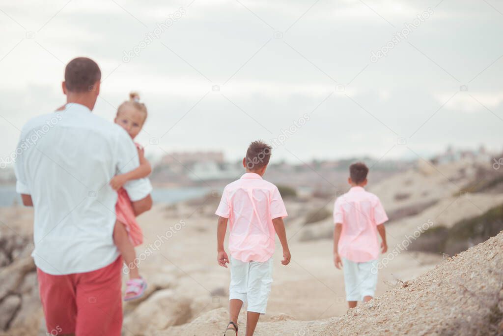 Big happy family walking at the beach. Dad and three children. The blue sky, the sun, fresh sea wind. Pleasure from nature and communication, outdoor