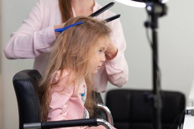 Parlak bir kuaförde saç stili üzerine çalışan kız, küçük, güzel bir modelden bukleler ve örgüler yapıyor.