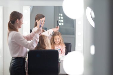 Parlak bir kuaförde saç stili üzerine çalışan kız, küçük, güzel bir modelden bukleler ve örgüler yapıyor.