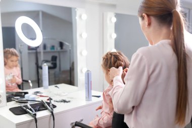 Parlak bir kuaförde saç stili üzerine çalışan kız, küçük, güzel bir modelden bukleler ve örgüler yapıyor.