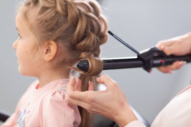Parlak bir kuaförde saç stili üzerine çalışan kız, küçük, güzel bir modelden bukleler ve örgüler yapıyor.