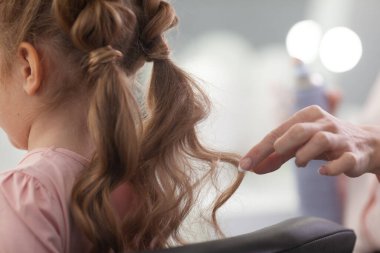 Parlak bir kuaförde saç stili üzerine çalışan kız, küçük, güzel bir modelden bukleler ve örgüler yapıyor.
