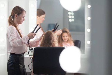 Parlak bir kuaförde saç stili üzerine çalışan kız, küçük, güzel bir modelden bukleler ve örgüler yapıyor.