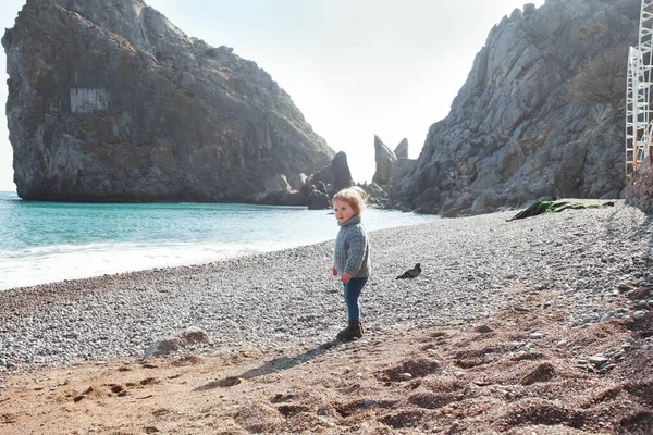 一个快乐的漂亮姑娘站在海边 背靠着大海和岩石 站在美丽的风景后面 小孩看着水 — 图库照片