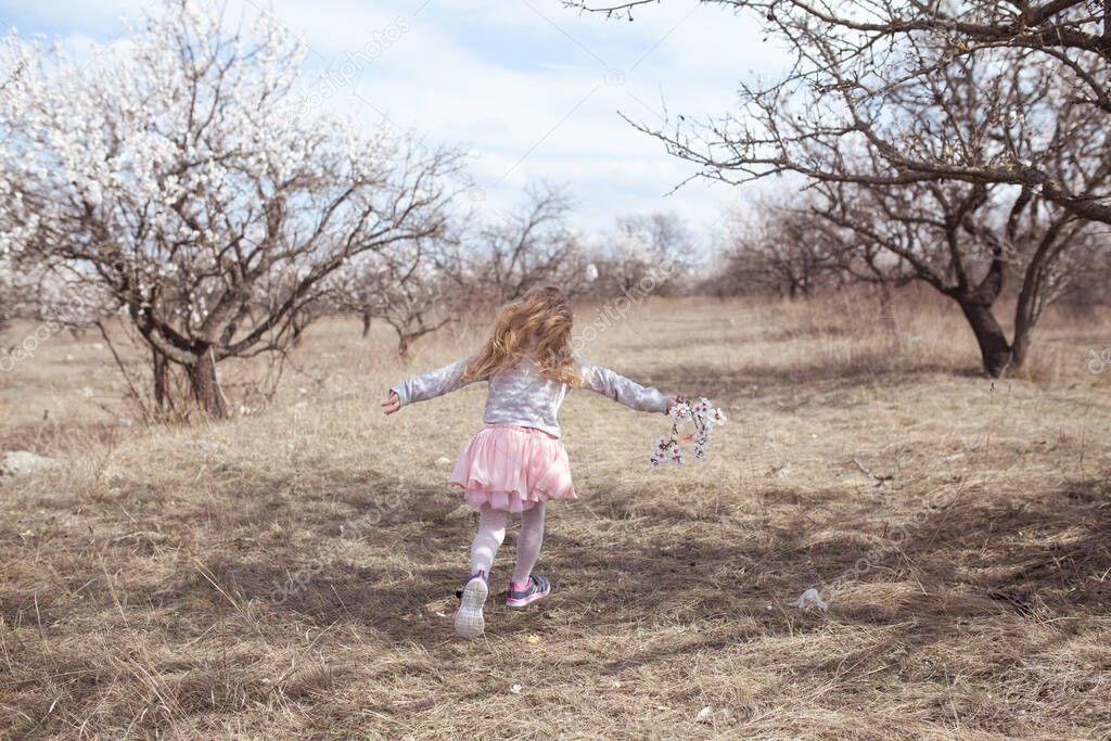 Happy beautiful girl runs and spins in a flowering almond garden, outdoor