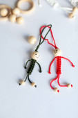 Red and green little men of thread on a white table, macrame