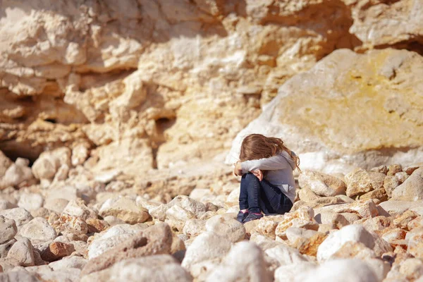一个悲伤的孩子坐在石头上 背靠岩石 一个女孩心烦意乱 哭泣着 站在室外 — 图库照片