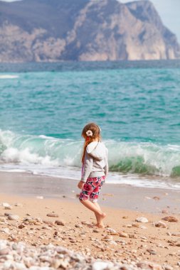 Mutlu güzel kız denizin arka planında güzel bir manzaranın arkasından deniz kıyısında yürüyor.