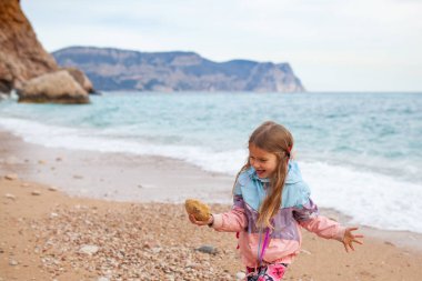 Mutlu güzel kız denizin arka planında güzel bir manzaranın arkasından deniz kıyısında yürüyor.