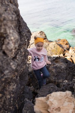 Mutlu çocuk deniz kıyısında yürüyor, bir kız taşlara tırmanıyor, açık havada.