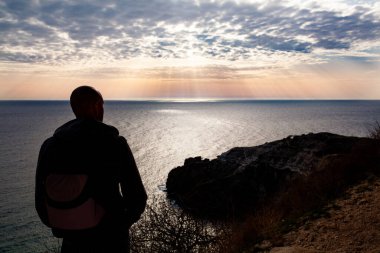 İnsan gezgin tek başına dağda duruyor ve sonbahar deniz manzarasına bakıyor. Soğuk mevsimde yürüyüş. Kavram sahnesi. Deniz ve uçurumun güzel panoramik manzarası, Karadeniz 'de bir dağ, manzara,