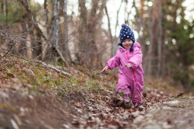 Küçük bir çocuk sonbahar ormanında yürür, pembe tulum ve şapka giyen bir kız, temiz orman havası çocukların sağlığı için iyidir,