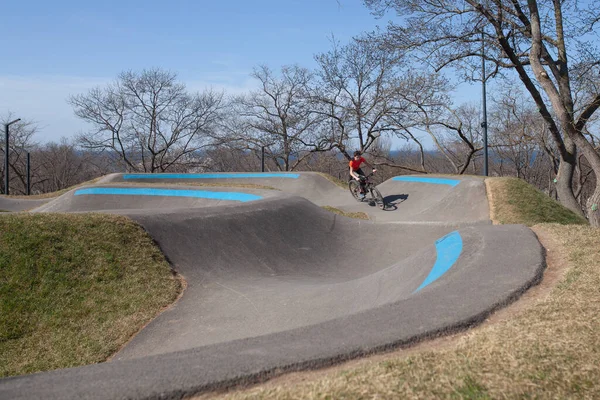 A teenager rides a bicycle on a pump track in a spring park, a guy goes in for sports