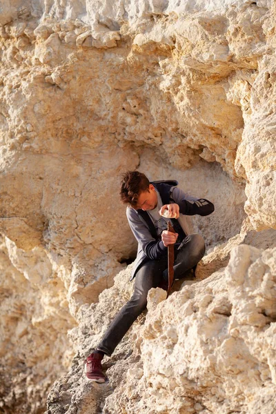 一个少年坐在石头上 在岩石中挖出石头 — 图库照片