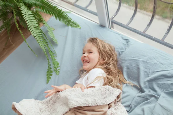 Šťastná Veselá Dívka Leží Modré Pohovce Okna Dítě Usmívá Pokoji — Stock fotografie