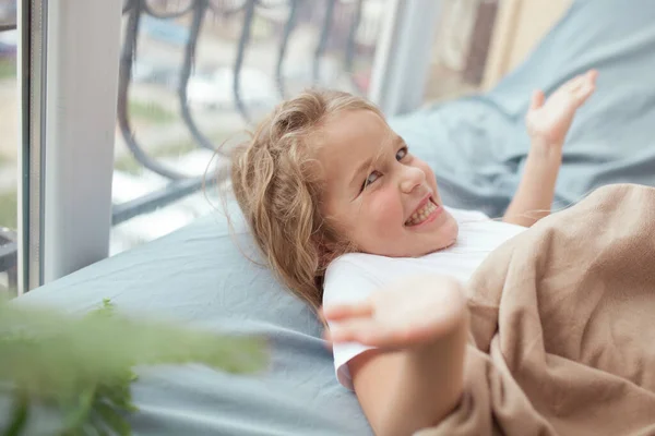 Šťastná Veselá Dívka Leží Modré Pohovce Okna Dítě Usmívá Pokoji — Stock fotografie