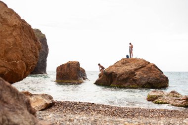 Gençler büyük bir kayanın üzerinde oturuyor ve denizde balık tutuyorlar. Denizde iki kardeşin boş vakitleri.